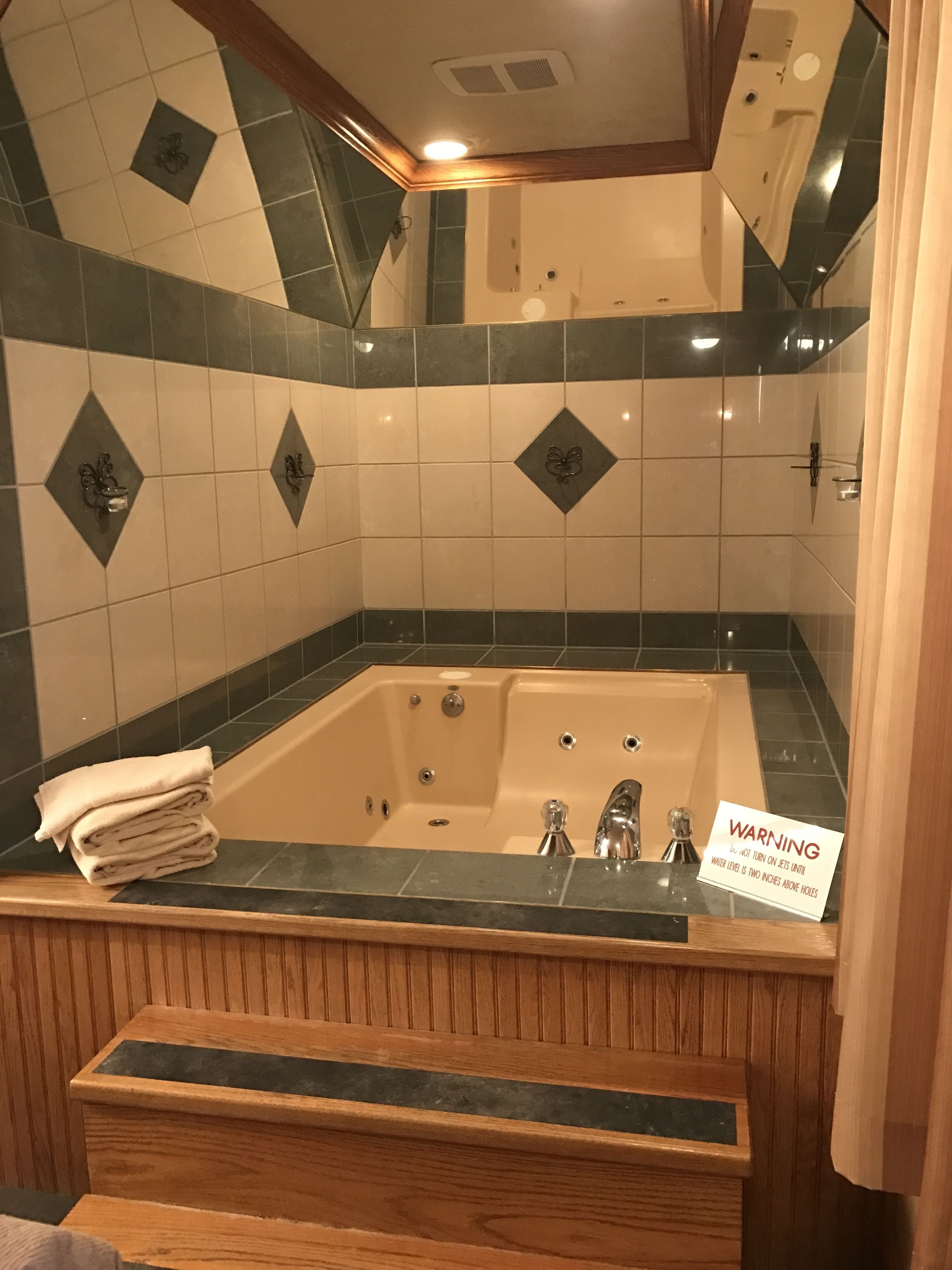 A bathroom with a large bathtub, a wooden vanity, and a warning sign about the water level.