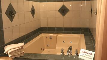 A bathroom with a large bathtub, a wooden vanity, and a warning sign about the water level.