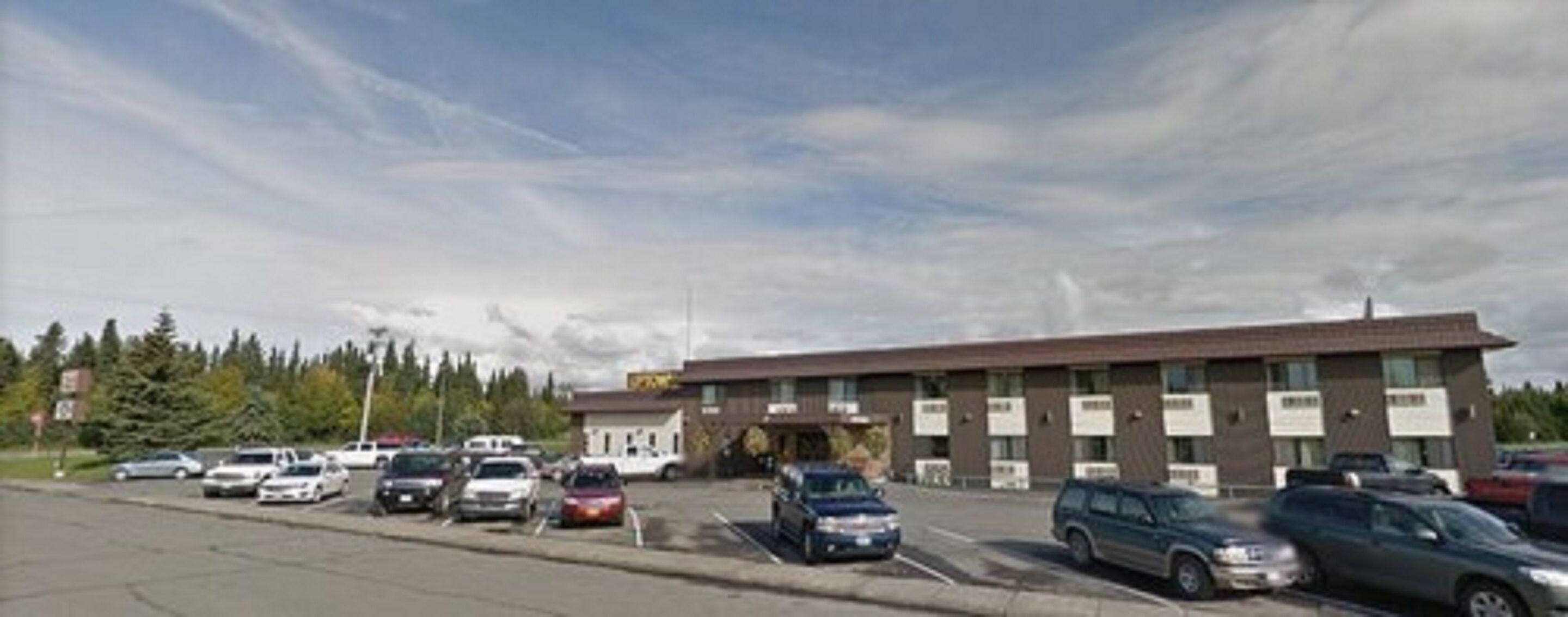 Un parking avec plusieurs voitures et un bâtiment doté de nombreuses fenêtres et de panneaux indicateurs.