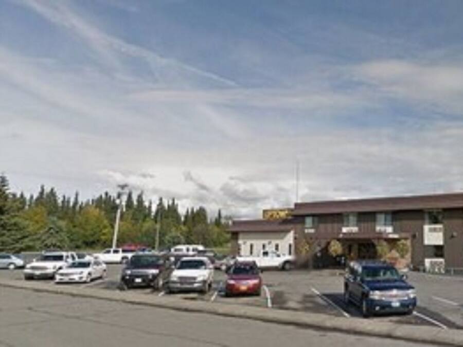 Un estacionamiento con varios automóviles y un edificio con múltiples ventanas y rótulos.