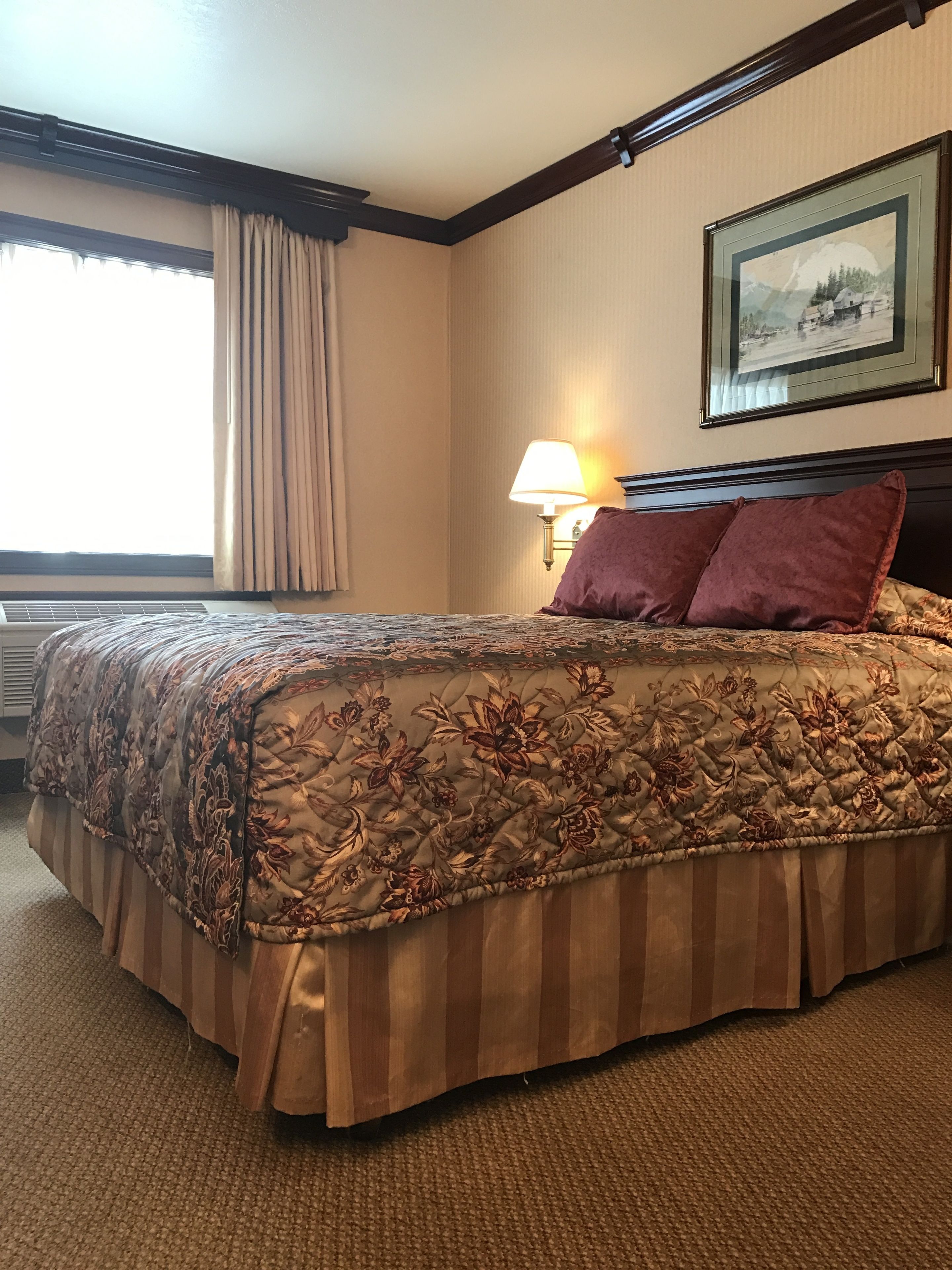 A hotel room with a large bed, a bedside lamp, a framed picture on the wall, and a window with curtains.