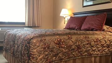 A hotel room with a large bed, a bedside lamp, a framed picture on the wall, and a window with curtains.