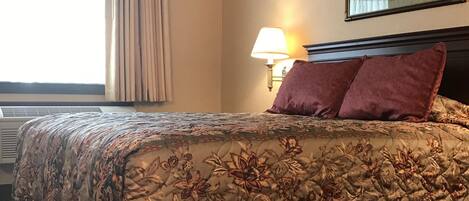 A hotel room with a large bed, a bedside lamp, a framed picture on the wall, and a window with curtains.