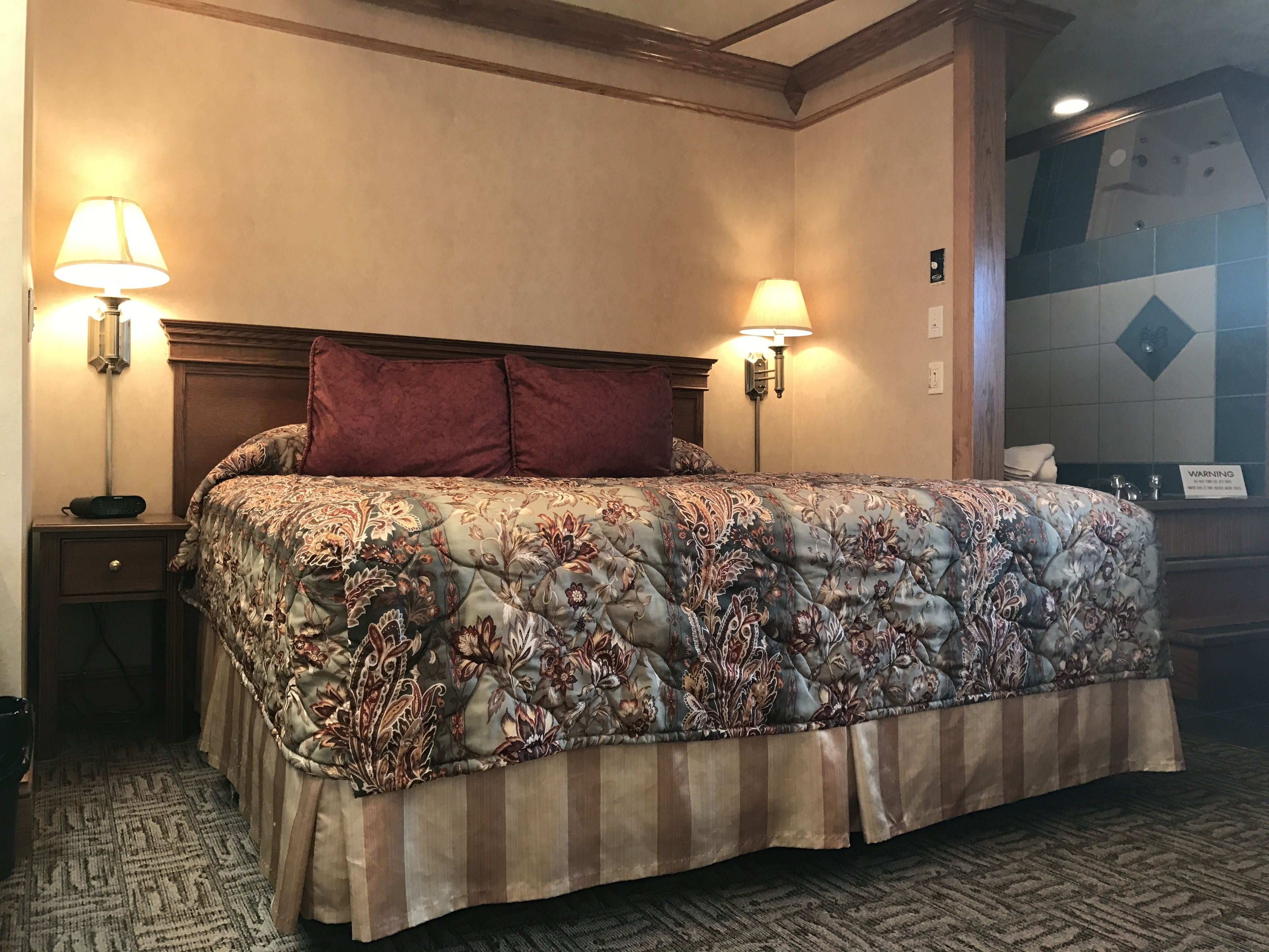 Ein Hotelzimmer mit einem großen Bett, zwei Nachttischlampen, einem Holzkopfteil, einem Teppichboden und einer Wand mit einem Warnschild.