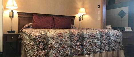 Ein Hotelzimmer mit einem großen Bett, zwei Nachttischlampen, einem Holzkopfteil, einem Teppichboden und einer Wand mit einem Warnschild.