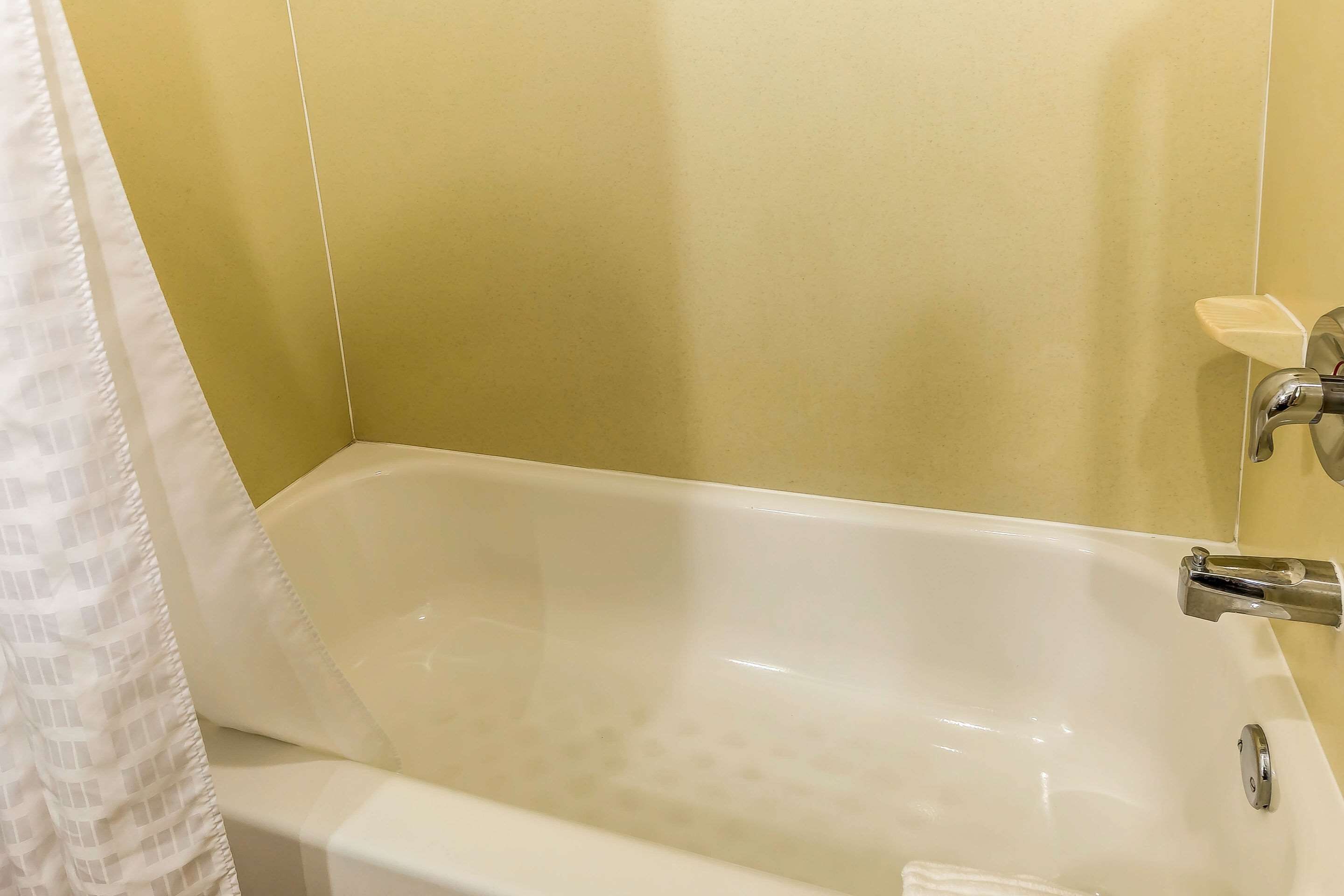 A bathtub with a chrome faucet, a white towel, and a soap dish on the wall.