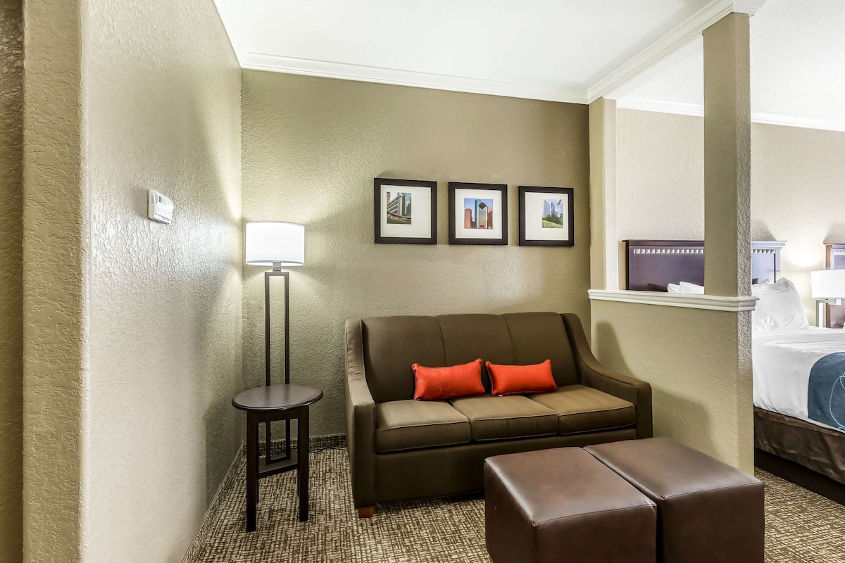 Una habitación de hotel con sofá, una mesita, cama y tres cuadros en la pared.