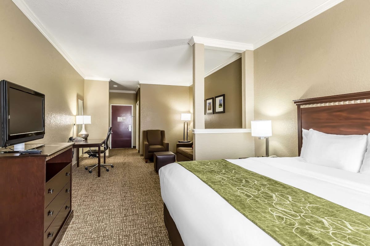 Habitación de hotel con cama, escritorio con televisor, silla y lámpara.