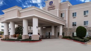 Un hotel con un letrero que dice 'Comfort Suites', una entrada techada y un cielo despejado.