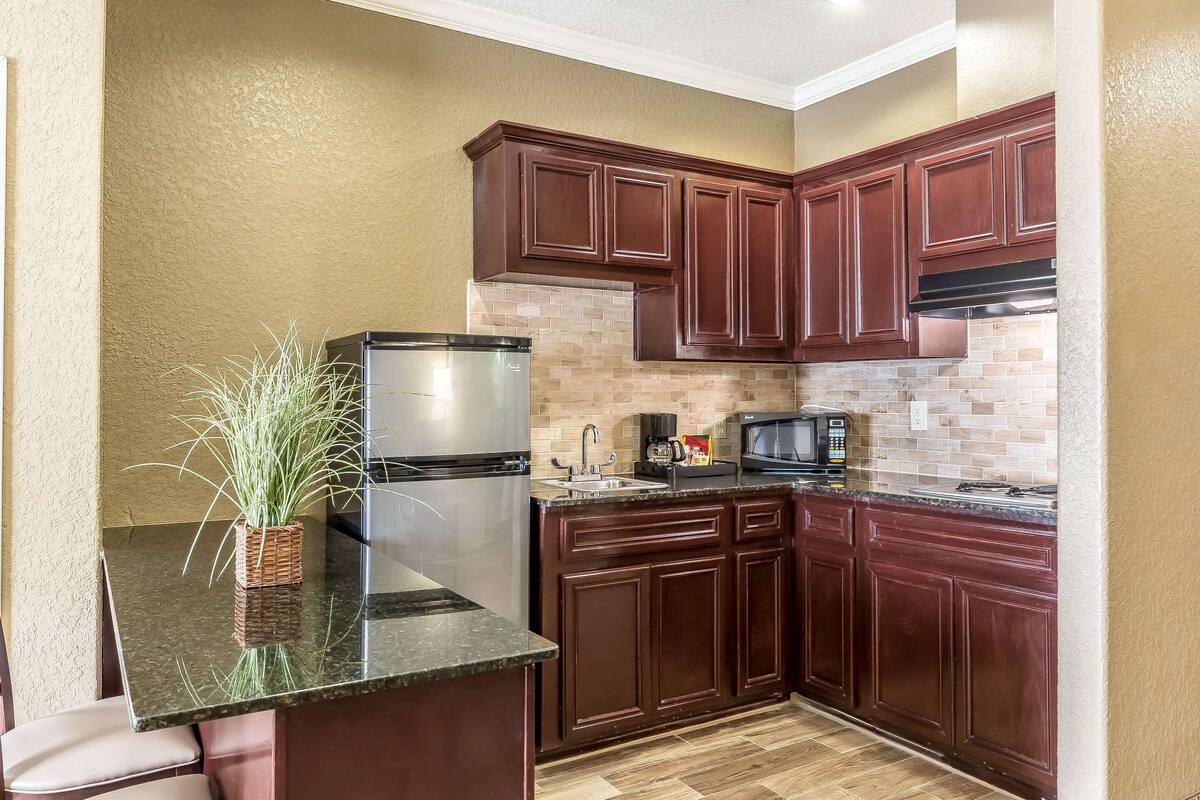 Una cocina con armarios de madera oscura, un refrigerador de acero inoxidable, un microondas y un salpicadero de azulejos.