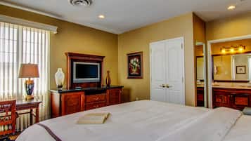 A hotel room with a large bed, a television, a desk with a lamp, a dresser, and a bathroom with a mirror and sink.