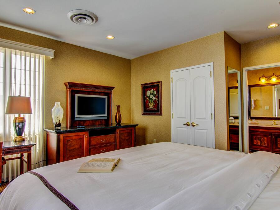 A hotel room with a large bed, a television, a desk with a lamp, a dresser, and a bathroom with a mirror and sink.