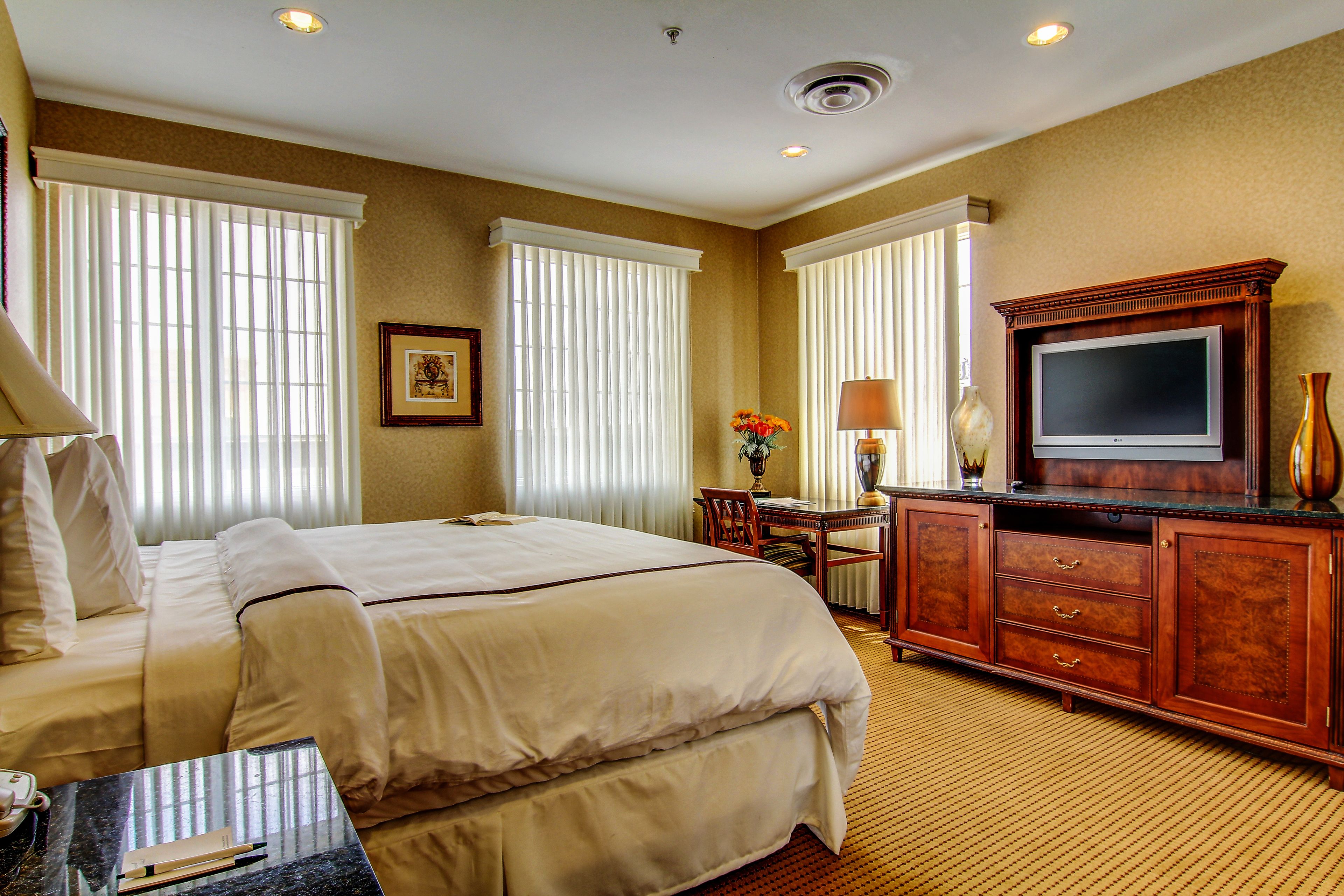 A hotel room with a large bed, a desk with a lamp, a television, and a vase with flowers.