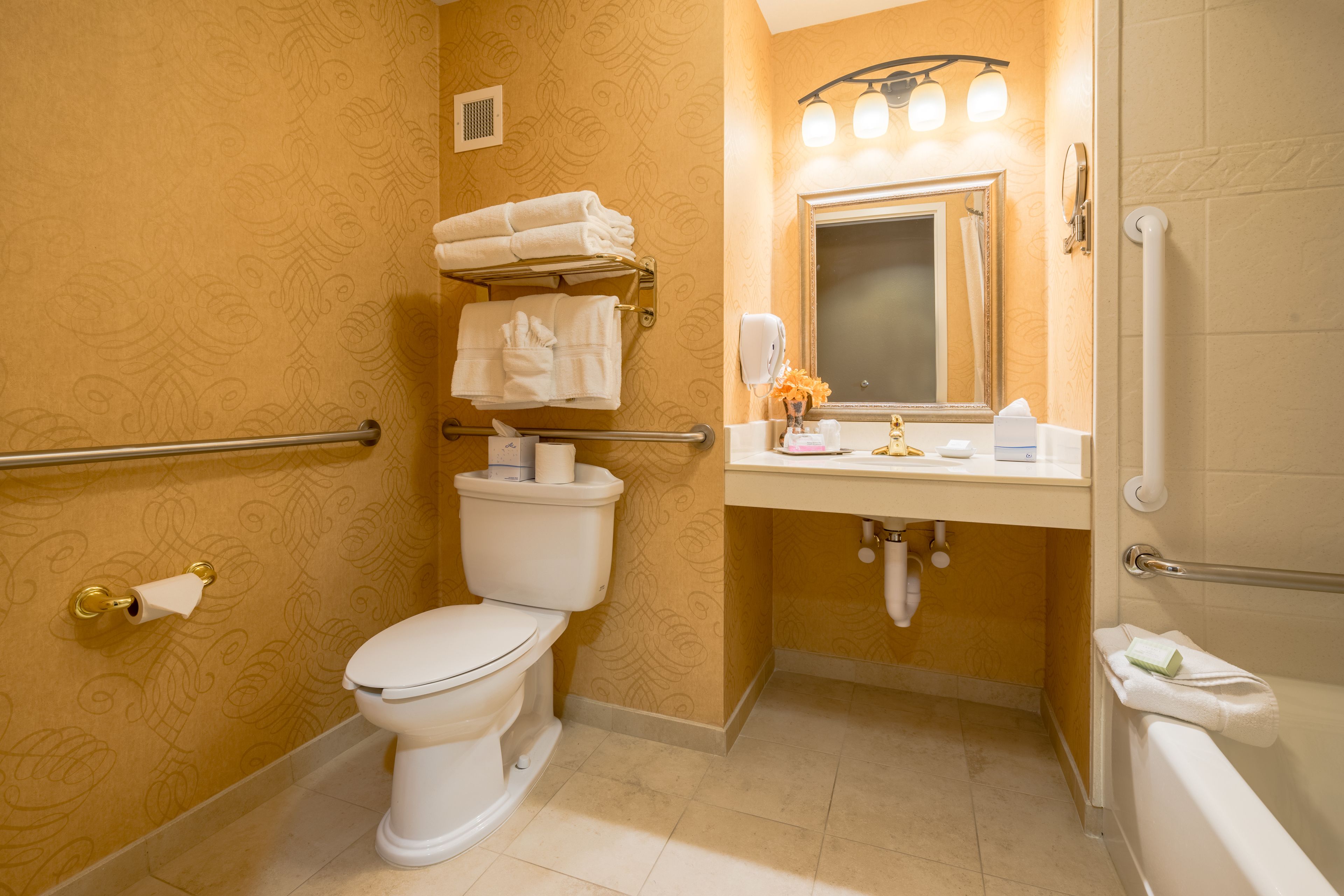 Un bagno con WC, lavandino e vasca da bagno. Asciugamani impilati su uno scaffale sopra il WC e un asciugamani ad aria montato sulla parete accanto al lavandino.