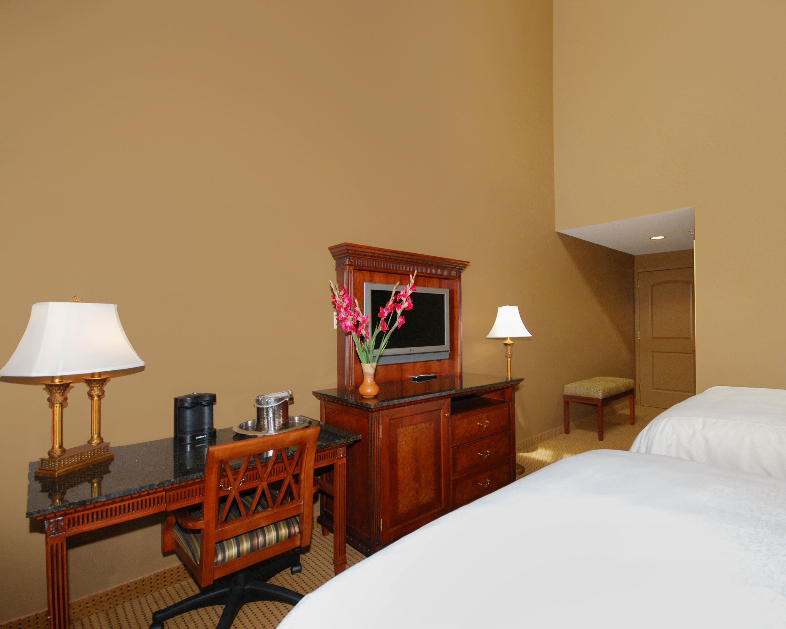 Ein Hotelzimmer mit Schreibtisch, zwei Lampen, Fernseher, Kommode und zwei Betten.