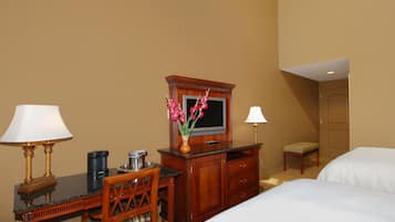 Ein Hotelzimmer mit Schreibtisch, zwei Lampen, Fernseher, Kommode und zwei Betten.