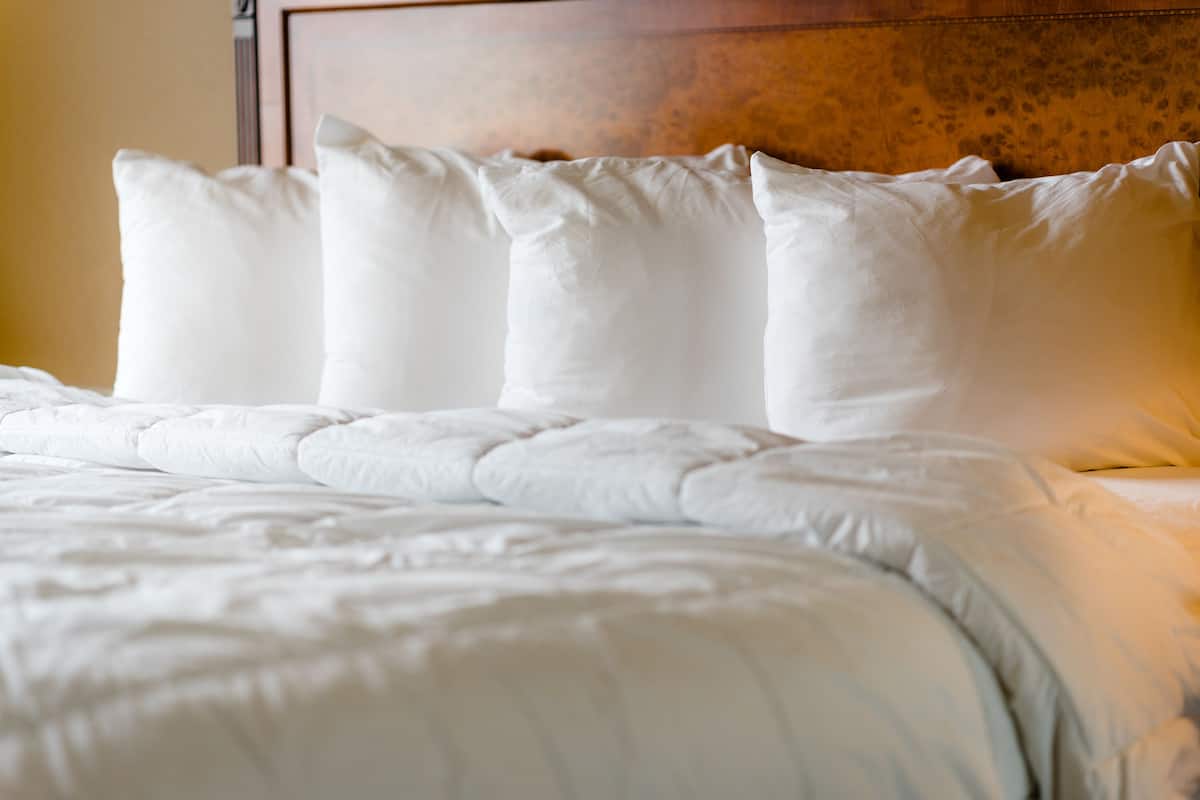 A neatly made bed with white bedding and a wooden headboard.