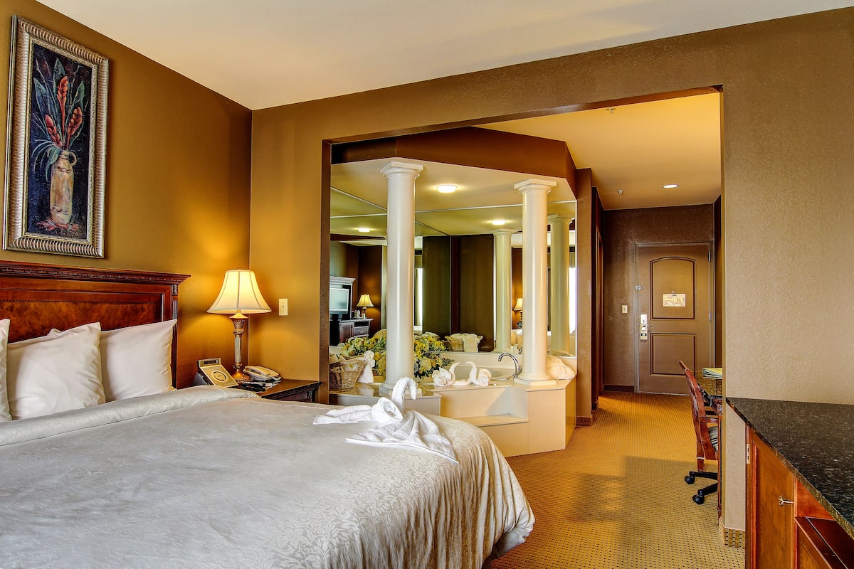 A hotel room with a large bed, a desk, a mirror, and a bathroom with a sink and toilet.