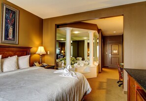 A hotel room with a large bed, a desk, a mirror, and a bathroom with a sink and toilet. - The Wildwood Hotel (Wildwood)