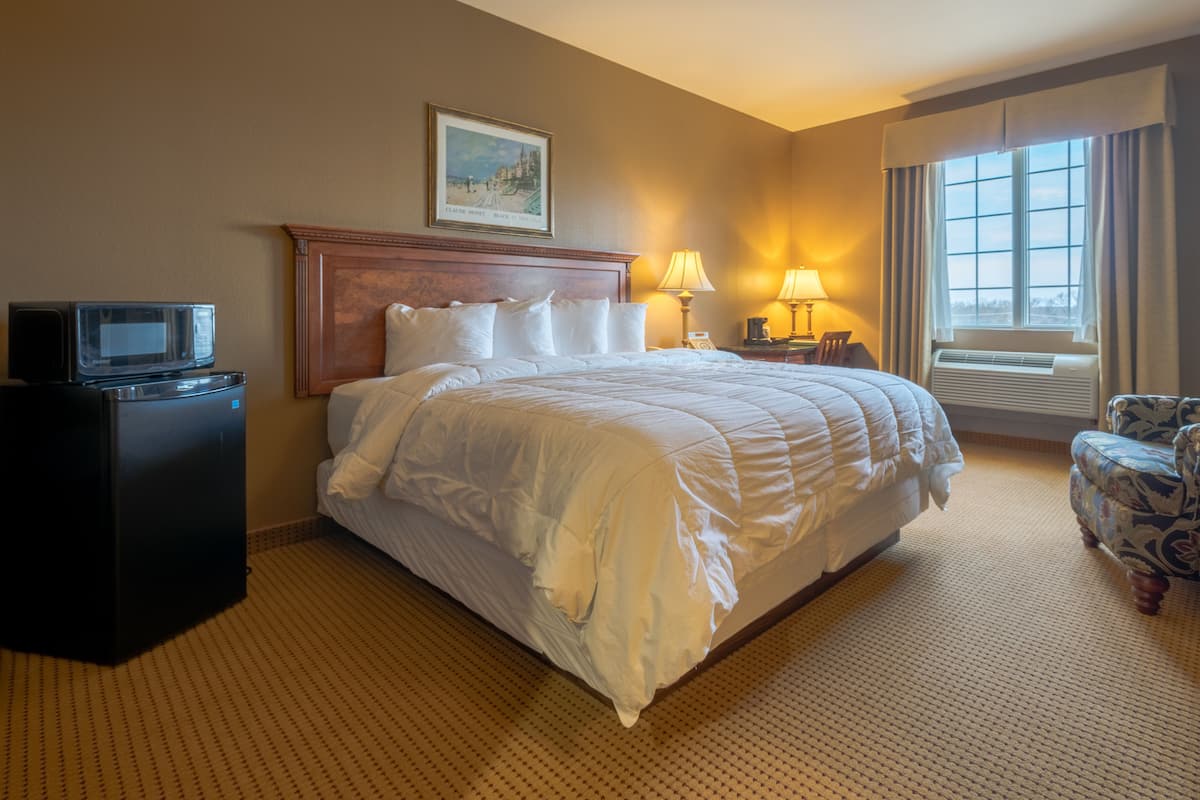 A hotel room with a large bed, a desk with a television, a chair, and a window with curtains.