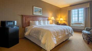 Habitación de hotel con una cama grande, un escritorio con televisor, una silla y un ventanal con cortinas.