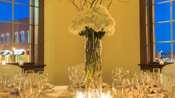 A table set for a formal dinner with a vase of flowers, candles, and a view of the cityscape through large windows.