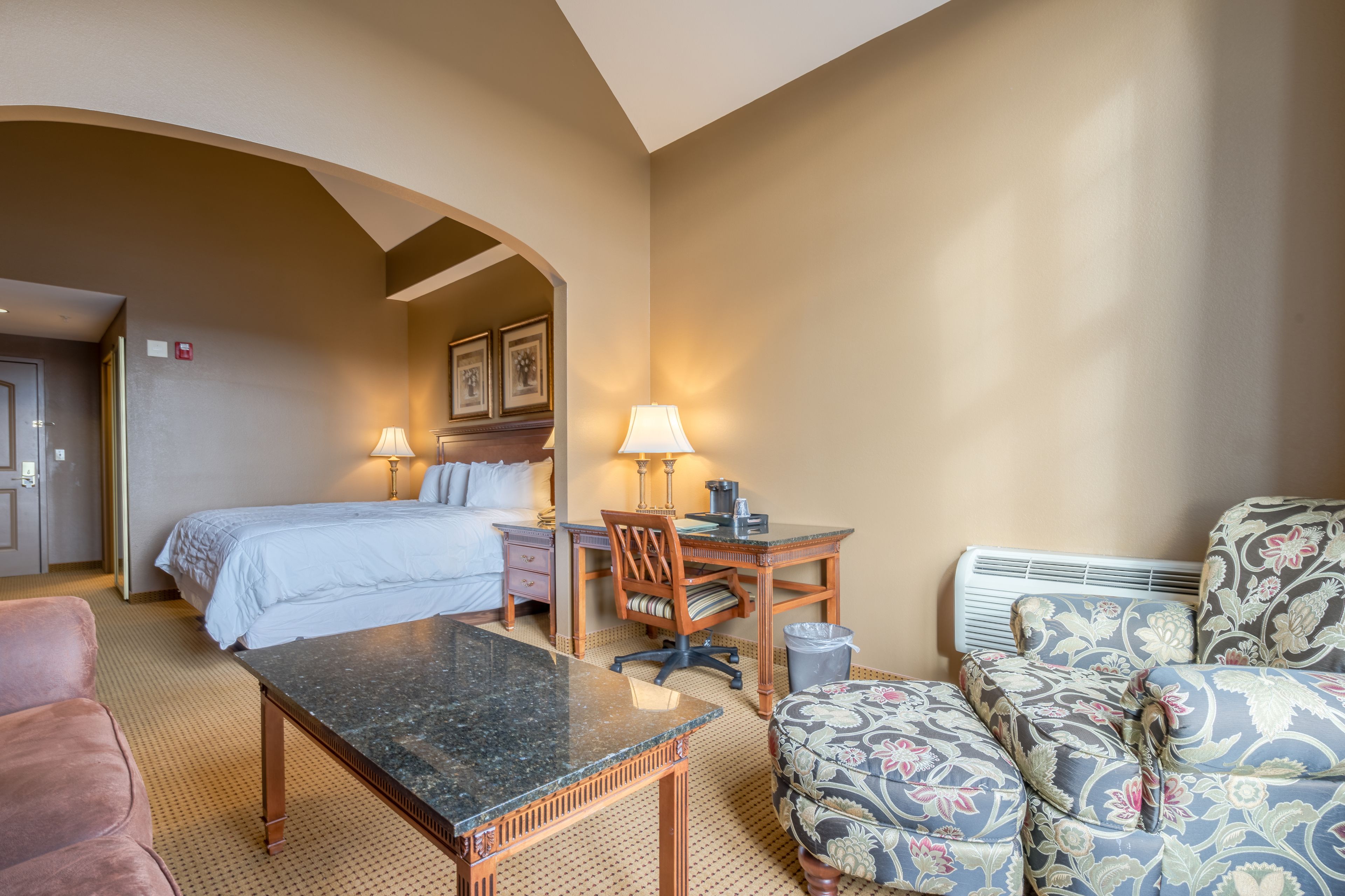 A hotel room with a bed, desk, chair, and a small table.