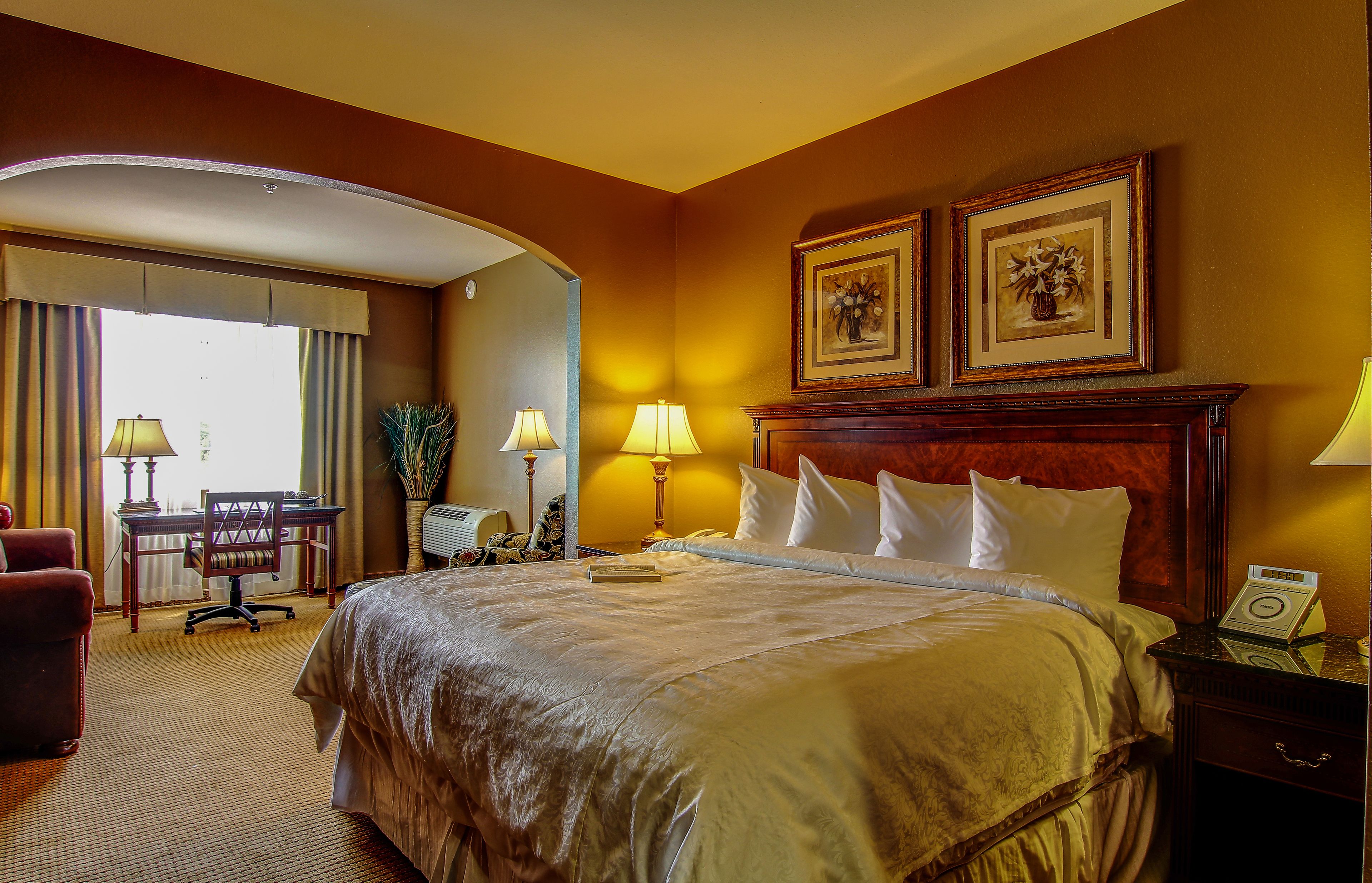 A hotel room with a large bed, two bedside tables, a desk with a chair, and a window with curtains.