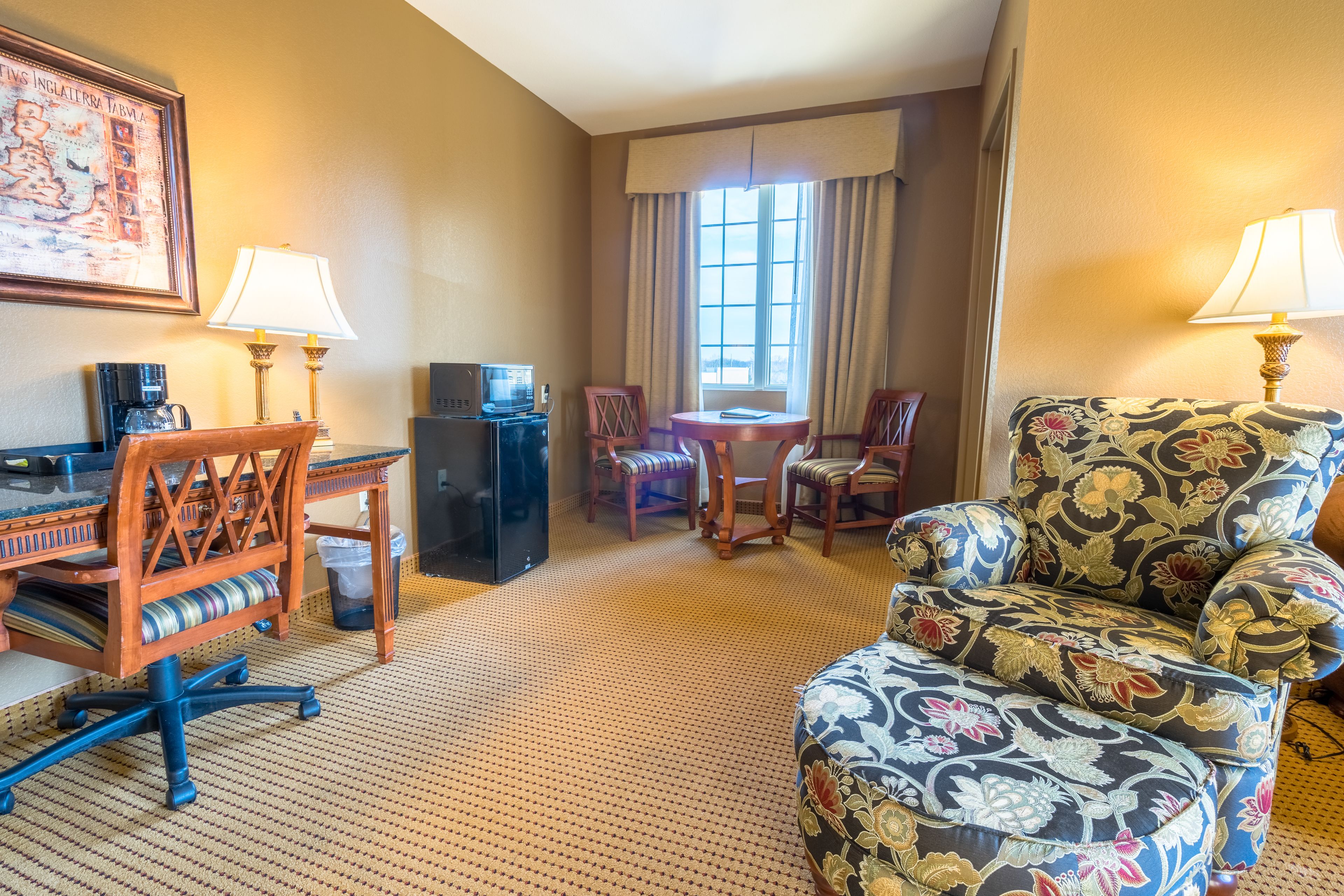 A hotel room with a desk, two chairs, a sofa, a small table, a TV, and a window with curtains.