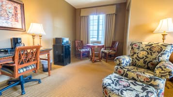 A hotel room with a desk, two chairs, a sofa, a small table, a TV, and a window with curtains.