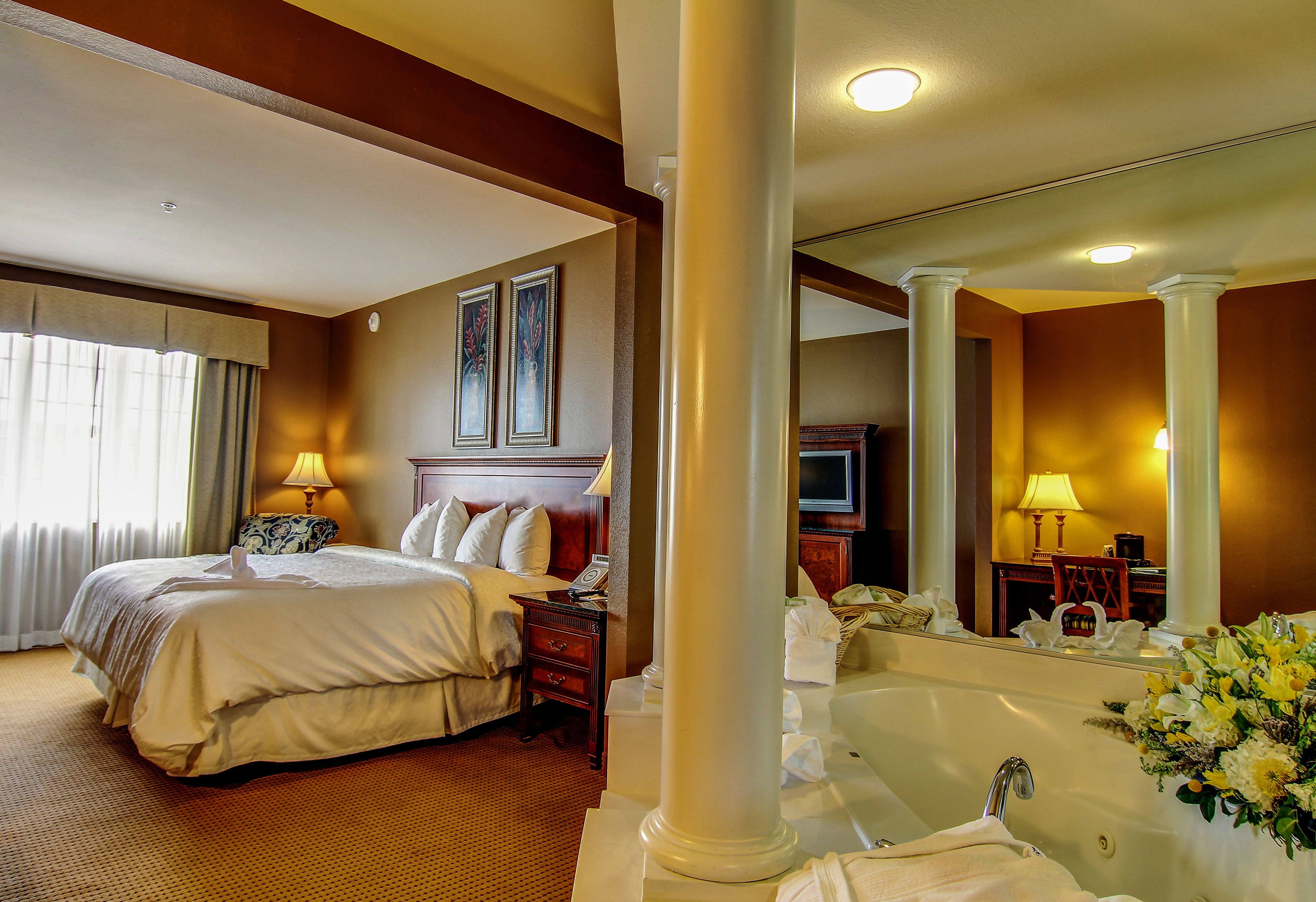 A hotel room with a large bed, a sitting area, a bathtub, and a television.