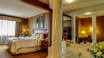 A hotel room with a large bed, a sitting area, a bathtub, and a television.
