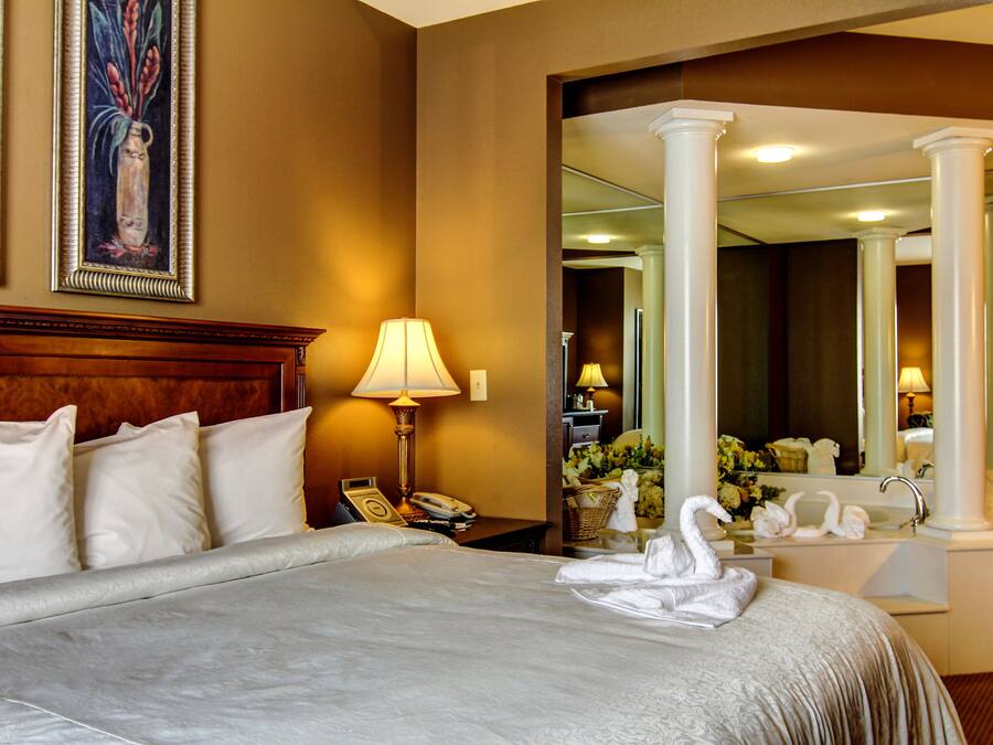 A hotel room with a large bed, a nightstand with a lamp, a telephone, and a mirror.