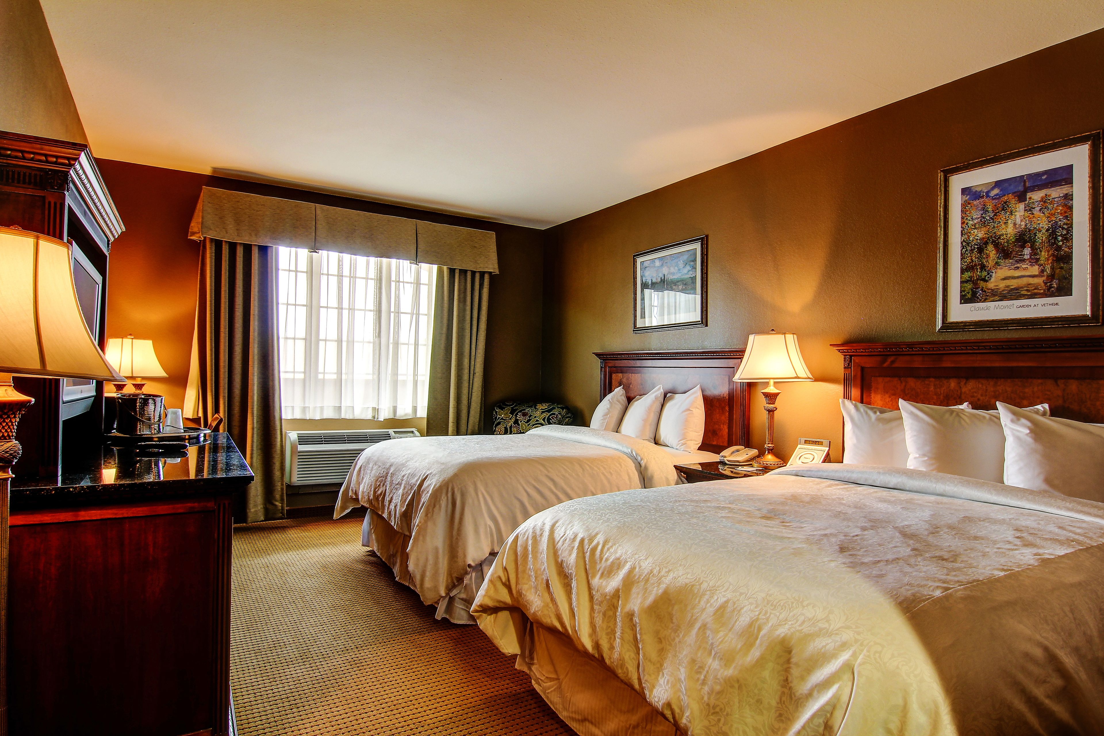 Une chambre d’hôtel avec deux lits, un bureau avec une lampe, une fenêtre avec des rideaux et un tableau au mur.