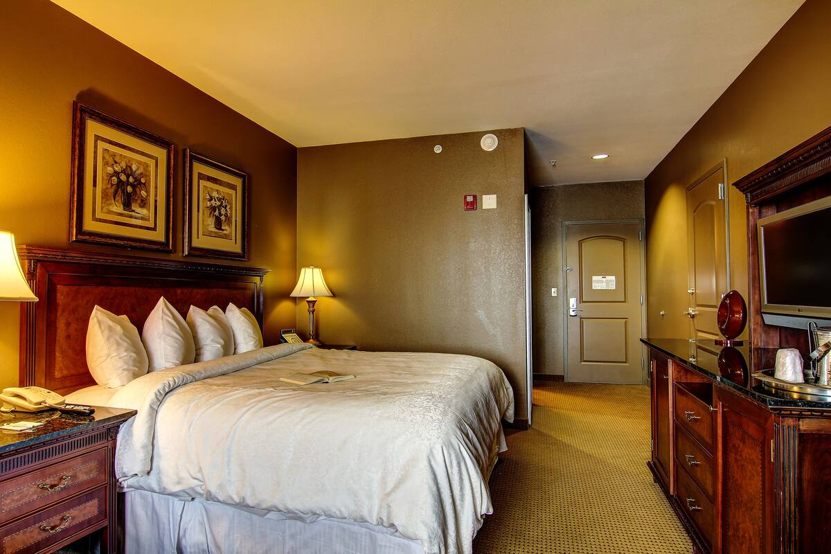 A hotel room with a large bed, bedside lamps, a dresser, a mirror, and framed artwork on the wall.