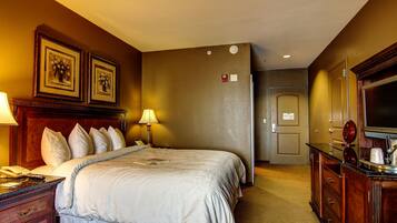 A hotel room with a large bed, bedside lamps, a dresser, a mirror, and framed artwork on the wall.