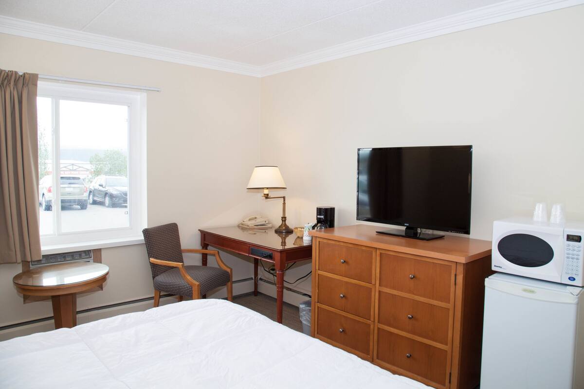 Habitación de hotel con cama, escritorio con silla, televisor, microondas y ventana con cortinas.