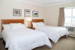 A hotel room with two beds, a nightstand with a lamp, and framed pictures on the wall. - Twin Pine Inn & Suites (Hinton)
