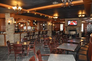 A restaurant with multiple tables and booths, a bar area, and a television screen mounted on the wall. - Twin Pine Inn & Suites (Hinton)