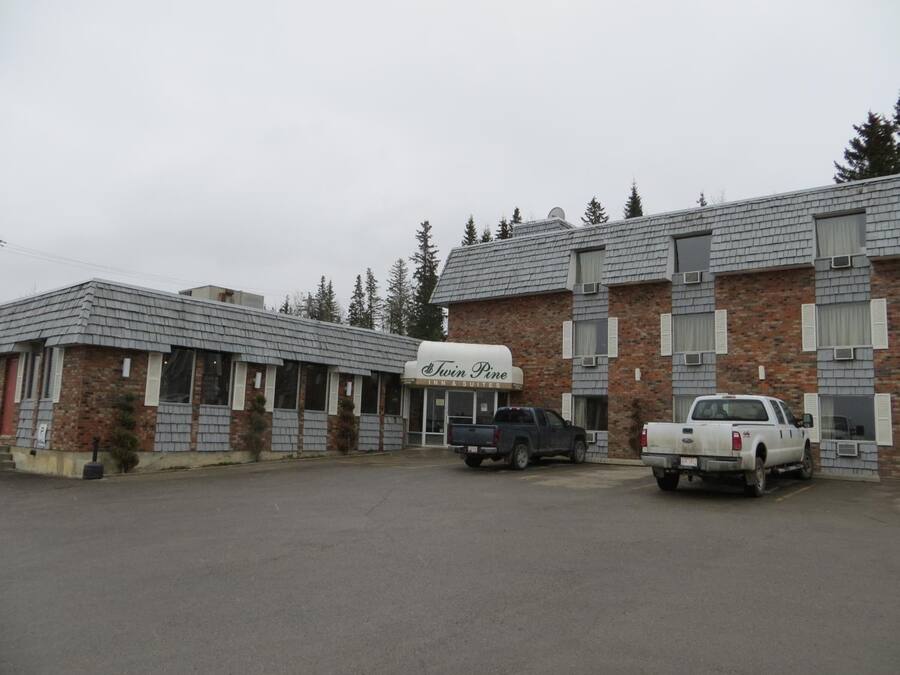 En toetages bygning med skilt for 'Twin Pine Inn & Suites'. To lastbiler er parkeret foran.