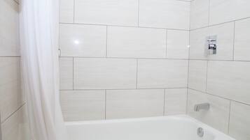 A modern bathroom with white tiles, a bathtub, and a shower curtain.