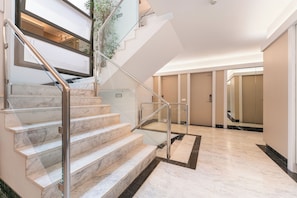 Vestíbulo de hotel con escaleras de mármol, barandilla de vidrio y diseño moderno.