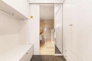 Un pasillo estrecho con un banco a la izquierda, una puerta que da a un baño y un armario con cajones a la derecha.