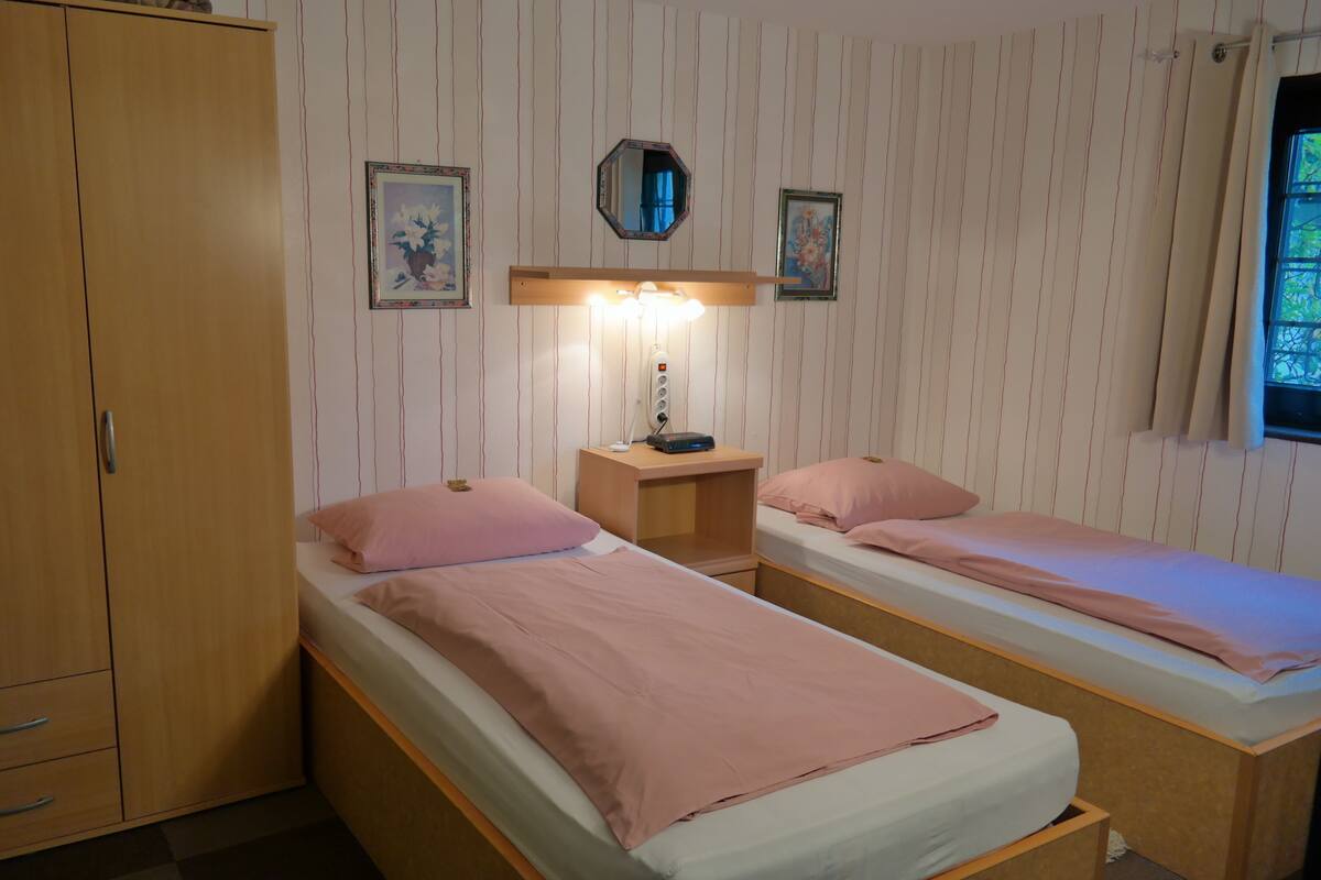 A room with two single beds, a wardrobe, a nightstand with a lamp, and a mirror on the wall.