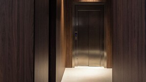 A modern elevator in a hallway with wooden walls and a light-colored floor. - Hotel California (Barcelona)