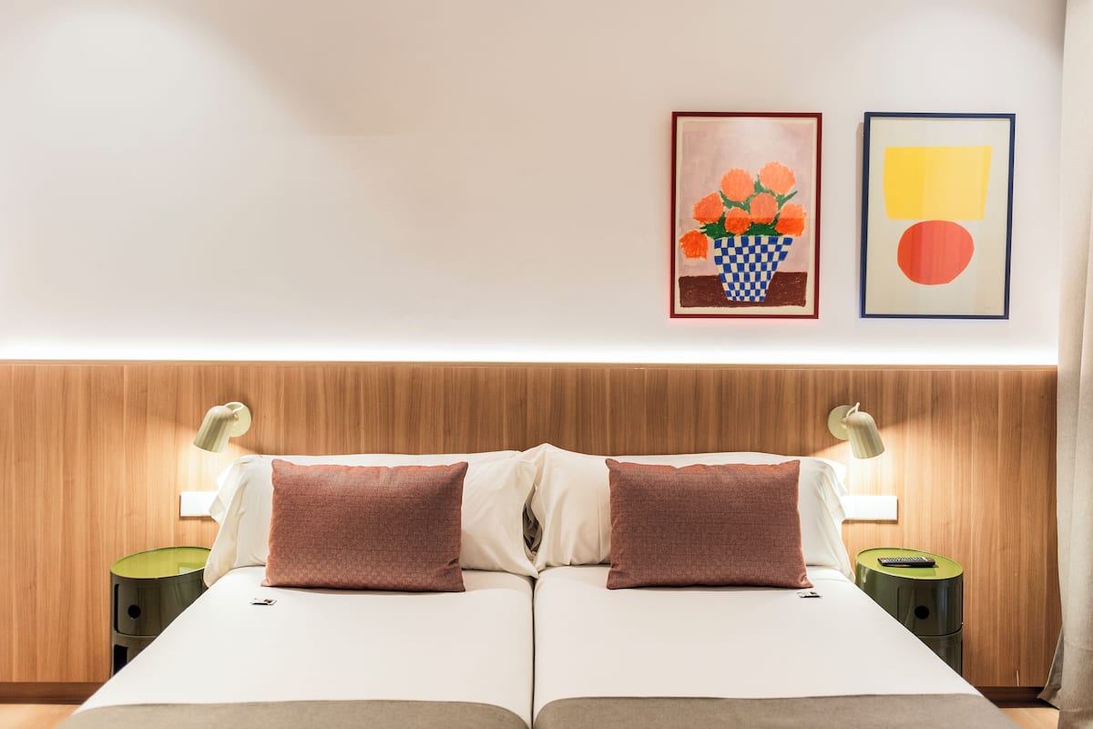 A double bed with two pillows, a bedside table with a lamp, and two framed artworks on the wall.