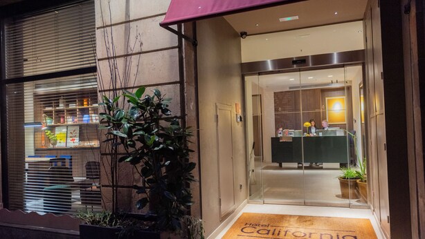 A hotel entrance with a reception desk, a glass door, and a doormat reading "Hotel California Barcelona". - Hotel California (Barcelona)