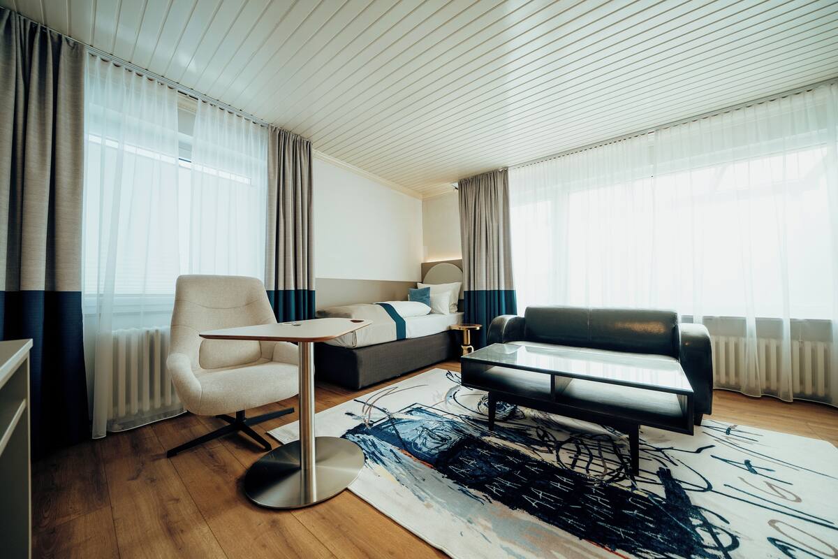 Een moderne hotelkamer met een bed, een bank, een bureau en een groot raam met gordijnen.