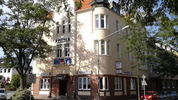 Et hotel med flere etager i klassisk europæisk arkitekturstil, med en markant hjørneindgang, mange vinduer og skilte med forskellige hotelnavne.