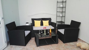 Un coin salon avec un canapé en rotin noir, deux fauteuils et une table basse en verre.